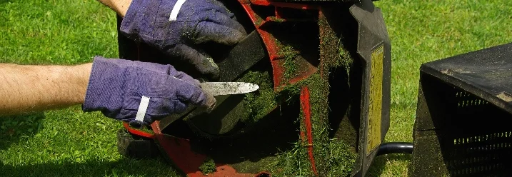 Person reinigt Rasenmäher mit Messer